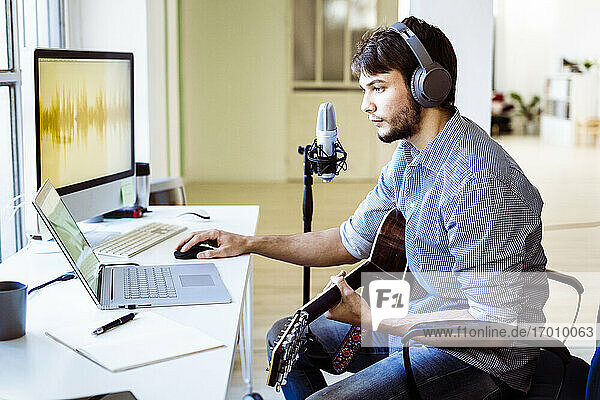 Profi mit Kopfhörern und Gitarre am Laptop im Aufnahmestudio