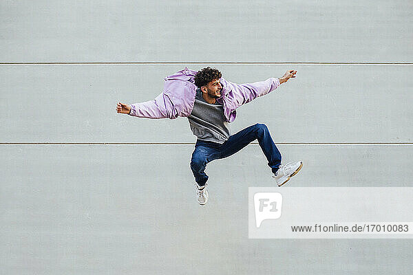 Young man jumping happily against wall