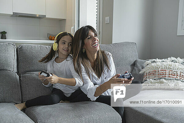 Smiling mother and daughter playing video games together at home