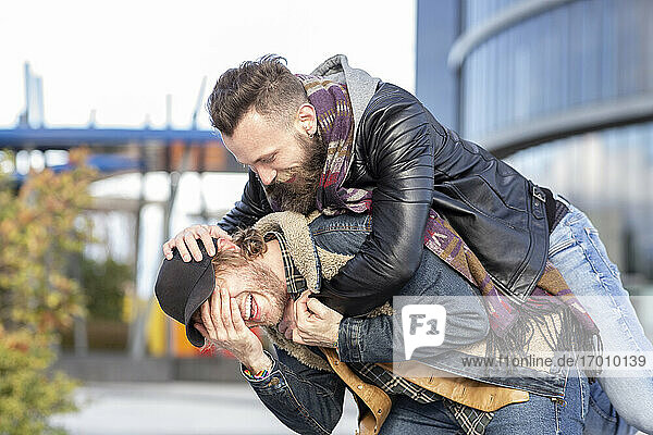 Playful boyfriend piggybacking gay man while standing in city