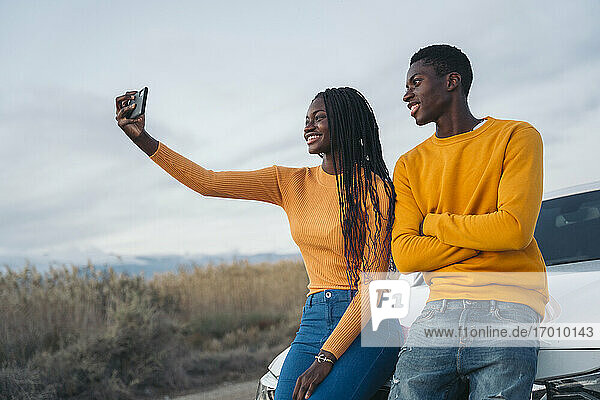Smiling couple talking selfie while leaning on wall