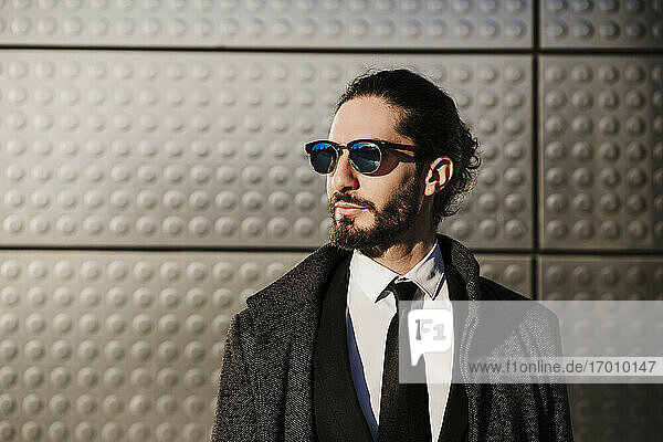 Geschäftsmann mit Jacke und Sonnenbrille schaut weg  während er vor einer silbernen Farbe steht