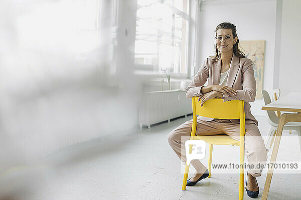 Porträt einer lächelnden Geschäftsfrau  die auf einem Stuhl im Büro sitzt