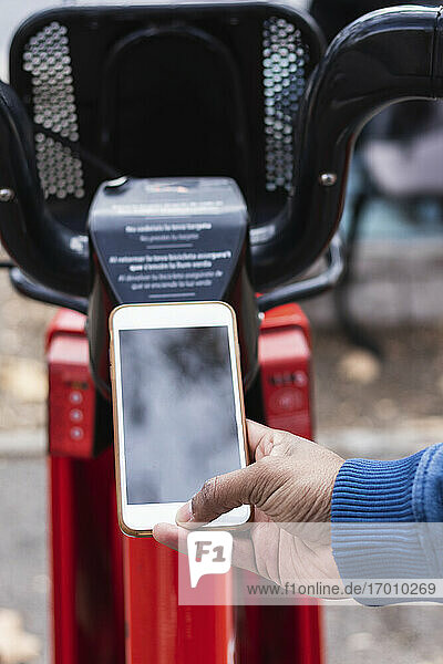 Hand eines Mannes  der an einer Parkstation über sein Smartphone ein Fahrrad ausleiht