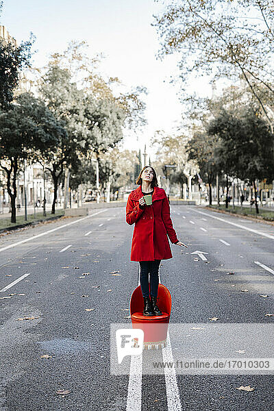 Junge Frau hält Kaffeetasse Tag träumt  während stehend auf Sitz an der Straße