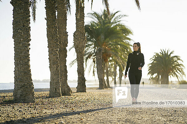 Junge Frau spaziert am Strand gegen den klaren Himmel bei Sonnenuntergang
