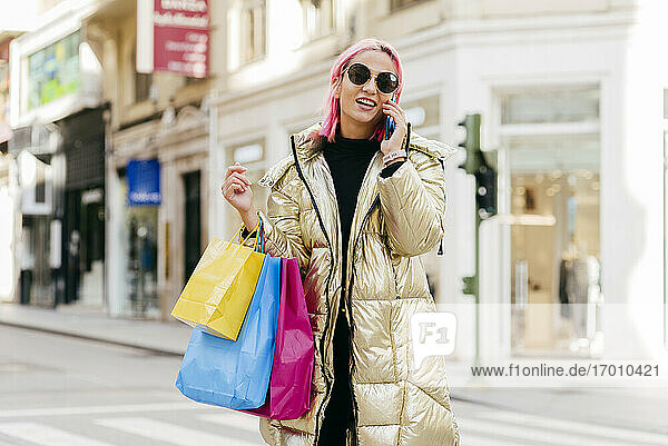 Junge modische Frau mit Einkaufstaschen  die in der Stadt mit ihrem Handy telefoniert