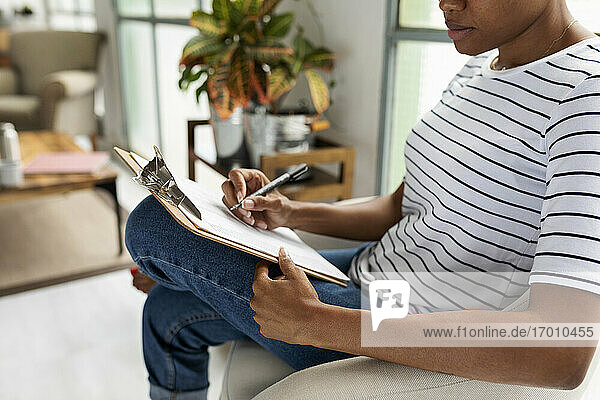 Frau sitzt auf einem Stuhl in einem legeren Büro und schreibt auf einem Klemmbrett