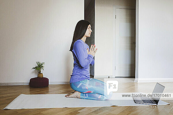 Mid adult woman learning yoga through laptop while sitting at home