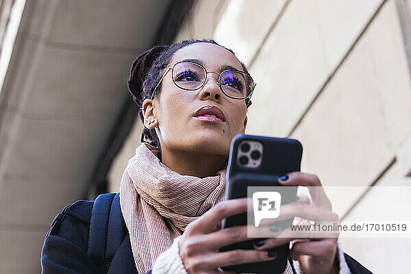 Schöne junge Frau schaut weg  während sie ein Smartphone hält