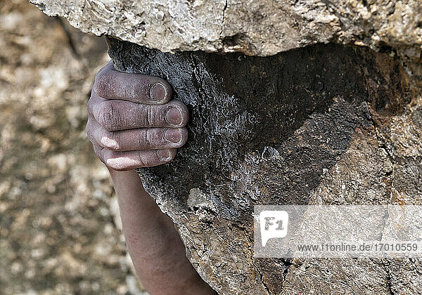 Hand eines jungen Mannes beim Klettern auf einen Felsen