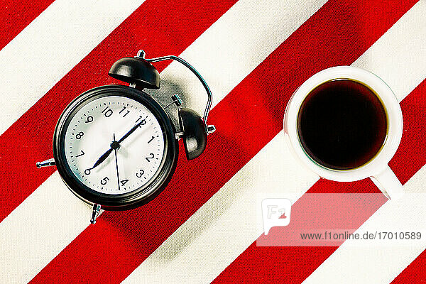 Kaffeebecher und Wecker auf weiß-rot gestreiftem Muster