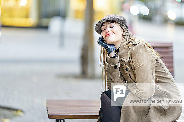 Smiling woman day dreaming while sitting on bench at footpath