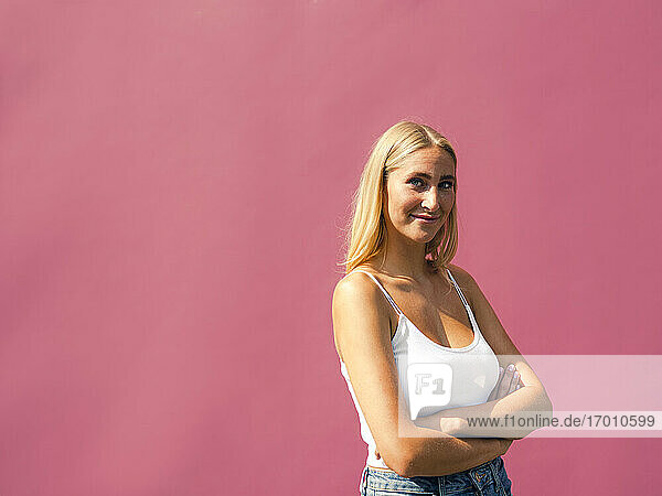 Lächelnde schöne Frau mit verschränkten Armen vor einer rosa Wand