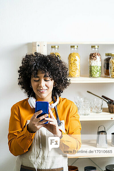 Curly hair woman using mobile phone while standing in kitchen at home