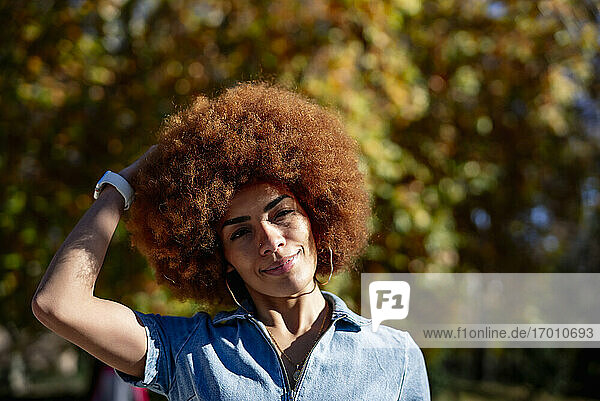 Lächelnde Frau mit Hand im Haar in einem öffentlichen Park