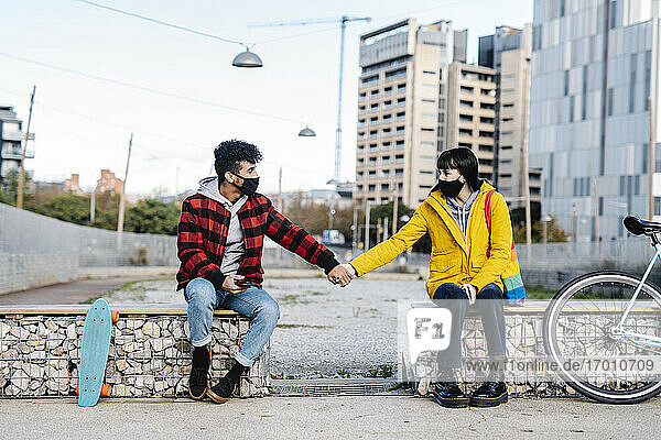 Paar mit Gesichtsschutzmaske hält sich auf einer Bank sitzend an den Händen