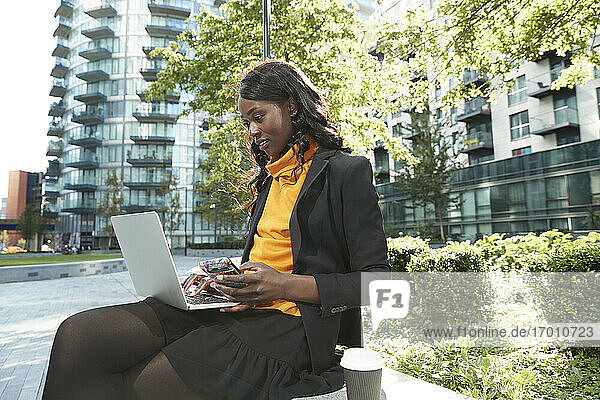Berufstätige Frau mit Mobiltelefon und Laptop im Büropark