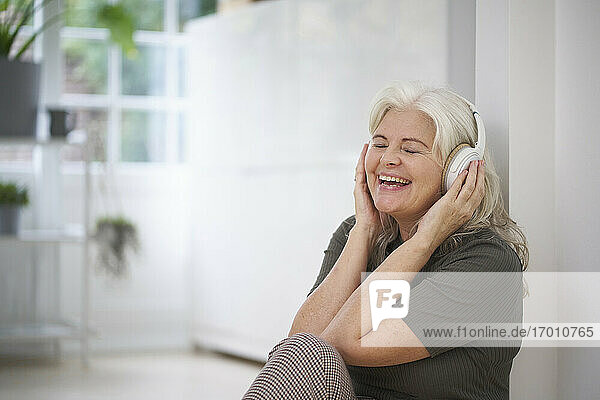 Glückliche ältere Frau  die in ihrer Wohnung Musik über Kopfhörer hört