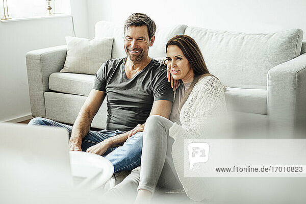 Mature man and woman watching movie on laptop while sitting on floor at home