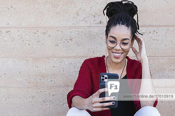 Lächelnde schöne junge Frau mit Dreadlocks nimmt Selfie gegen Wand