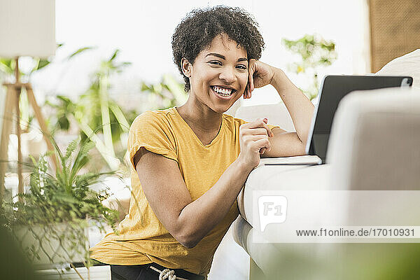 Lächelnde Frau  die ein digitales Tablet benutzt  während sie zu Hause sitzt