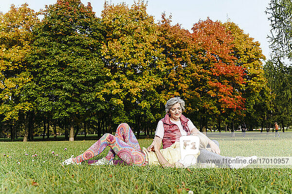 Reife Frau liegt auf dem Schoß ihrer Freundin auf dem Rasen im Herbstpark