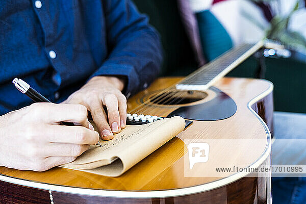Songschreiber schreibt Musik auf einem Notizblock  während er mit einer Gitarre im Studio sitzt