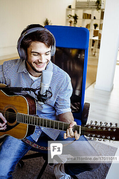 Smiling musician recording music while playing guitar at recording studio