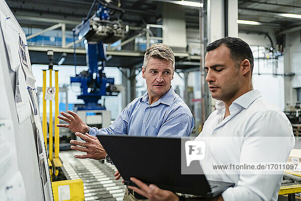 Male supervisor looking at manager while using laptop in meeting at factory