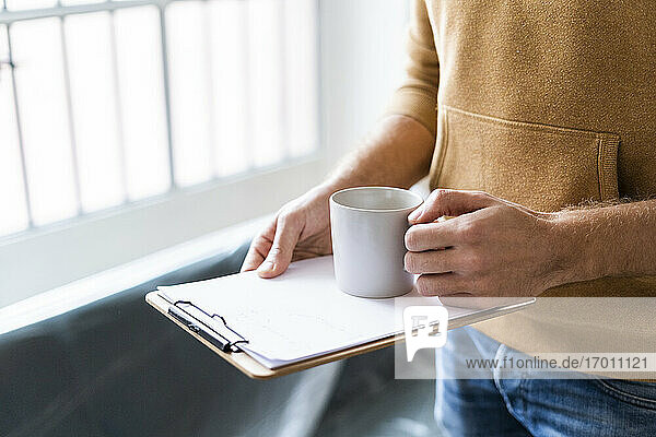 Junger Mann mit Kaffeetasse  Klemmbrett und Papier im neuen Zuhause
