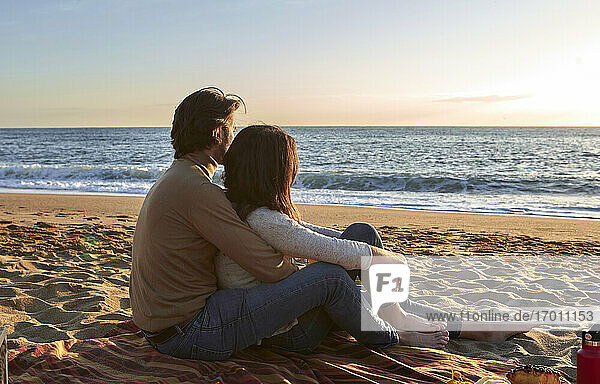 Junges Paar mit Blick auf das Meer am Strand sitzend