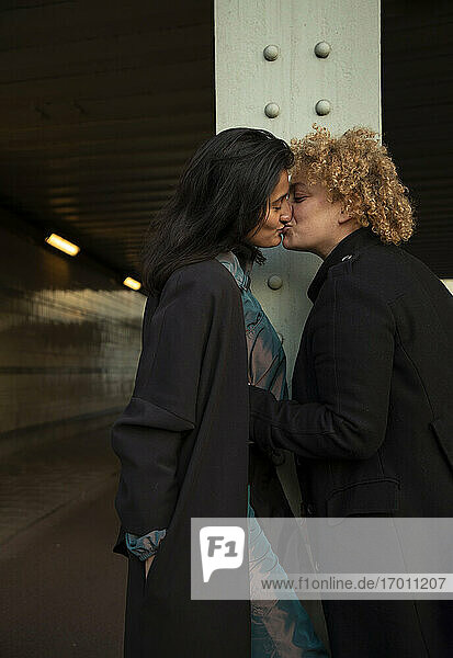 Lesbian couple kissing under bridge at night