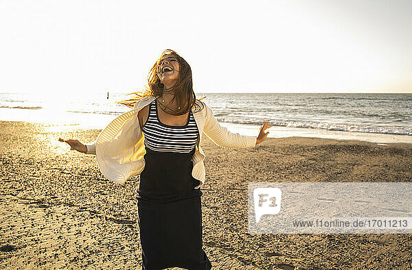 Fröhliche Frau tanzt am Strand gegen den Himmel an einem sonnigen Tag