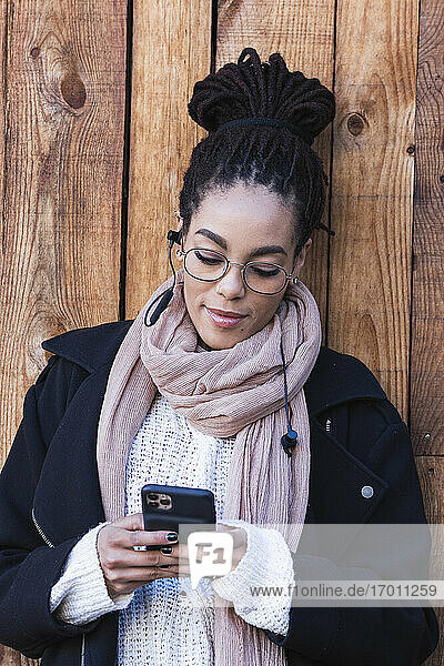 Schöne junge Frau benutzt ihr Smartphone und lehnt sich an eine Holzwand