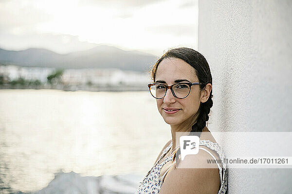 Mittlere erwachsene Frau mit Brille  die sich bei Sonnenuntergang an eine weiße Wand lehnt