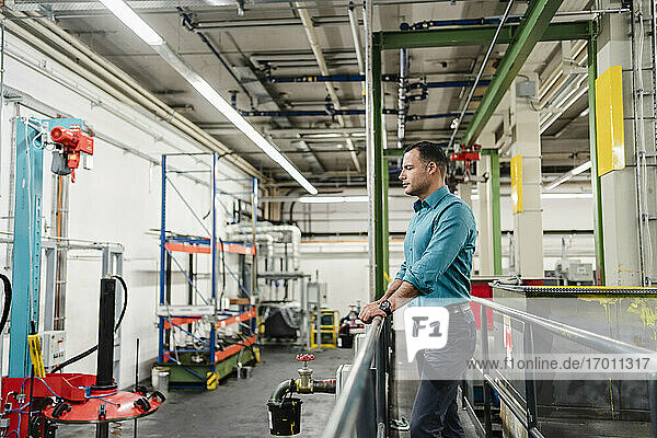 Mature supervisor overlooking machinery while standing in factory