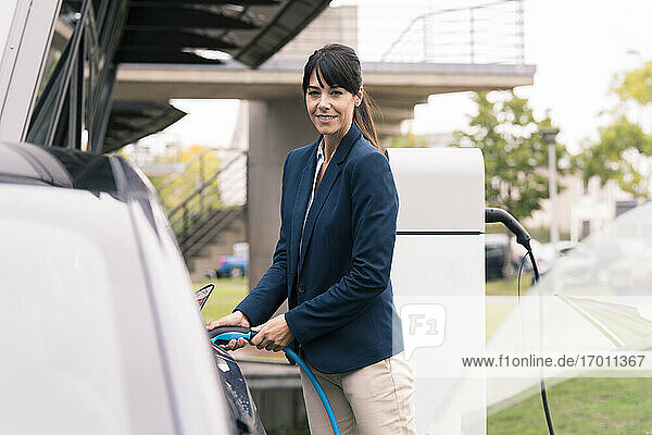 Lächelnde Unternehmerin beim Einstecken des Ladegeräts in ein Elektroauto