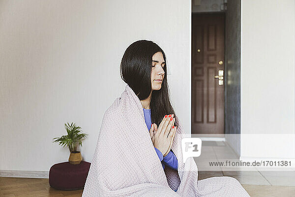 Woman covered in blanket meditating while sitting at home