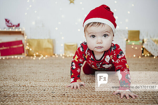 Niedliches kleines Mädchen mit Weihnachtsmannmütze krabbelt auf dem Boden zu Hause während Weihnachten