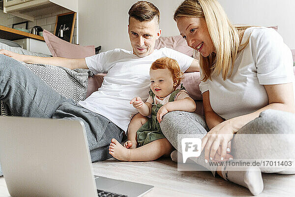 Glückliche Familie mit kleiner Tochter  die zu Hause auf den Laptop schaut