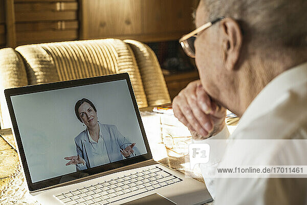 Ärztin für Allgemeinmedizin berät einen männlichen Patienten während eines Videogesprächs im Wohnzimmer