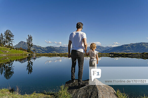 Father standing with little daughter on top of lakeshore boulder