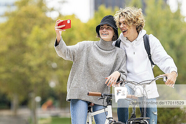 Glückliche Frau  die ein Selfie macht und neben einem männlichen Freund mit Fahrrad im Park steht