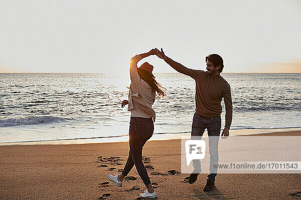 Happy young couple dancing while standing at beach during sunrise
