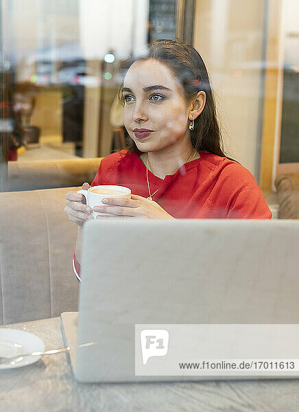 Junge Frau mit Kaffeetasse durch Glas im Café gesehen