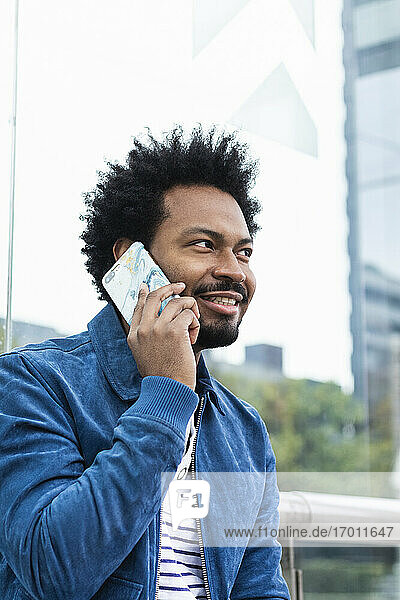 Nahaufnahme eines stilvollen Mannes mit Afro-Haar  der im Freien sitzend über ein Smartphone spricht