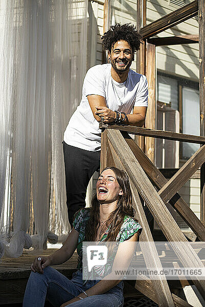 Smiling man standing by cheerful woman sitting on staircase