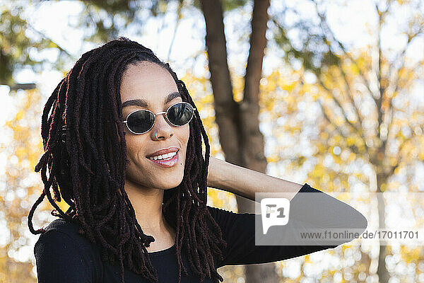 Fashionable young woman with dreadlocks wearing sunglasses at park