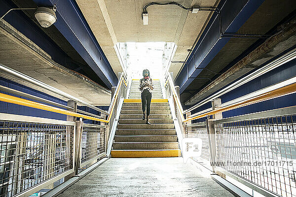 Geschäftsfrau  die ein Mobiltelefon benutzt  während sie auf einer Treppe in einer U-Bahn-Station geht